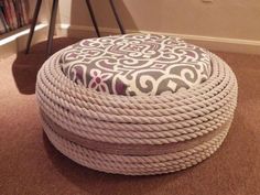 a white rope covered ottoman sitting on top of a carpeted floor next to a book shelf