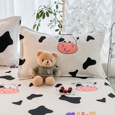 a teddy bear sitting on top of a bed next to two pillows with cow designs