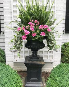 a black urn filled with pink flowers sitting in front of a white brick building