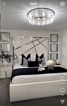 a white bed sitting under a chandelier next to a mirror and table with flowers on it