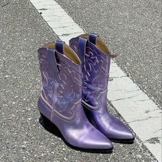 a pair of purple cowboy boots sitting on the side of a road next to a curb