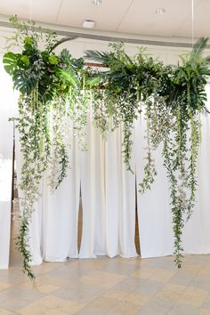 an arrangement of greenery is hanging from the ceiling in front of white drapes