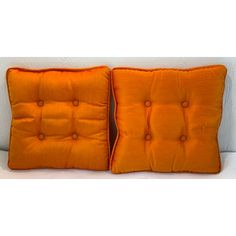 two orange pillows sitting on top of a white couch next to each other with buttons