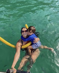 a woman holding a child on her back in the water with a life preserver