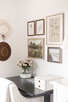 a black table topped with a vase filled with flowers next to pictures on the wall