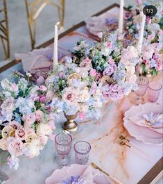 the table is set with pink and blue flowers, candles, and napkins on it