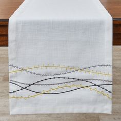 an embroidered table runner with yellow and black lines on white linen, sitting on a wooden table