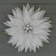 a white wreath with pearls and green leaves on the side of a house, ready to be decorated for christmas