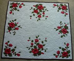 a white quilt with red flowers on it sitting on the floor next to a wall