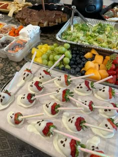 a table topped with lots of fruit and desserts next to bowls of salad on sticks