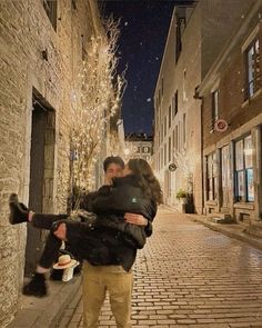 a man and woman hug on the street in front of a brick building at night