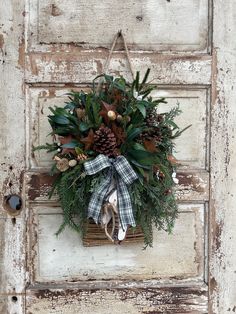 a wreath with pine cones and evergreens hangs on an old door