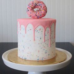 a white cake with pink frosting and sprinkles on top is sitting on a pedestal