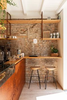 a kitchen with brick walls and wooden shelves, two stools in front of the counter