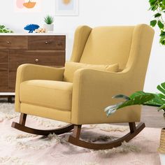 a yellow rocking chair sitting on top of a rug next to a dresser and potted plant