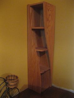 a wooden book shelf next to a bicycle in a room with yellow walls and wood flooring