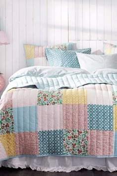 a bed with colorful quilts and pillows on top of it in a white room