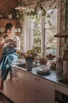 a woman sitting on top of a kitchen counter next to a window