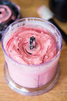 a blender filled with pink frosting on top of a wooden table