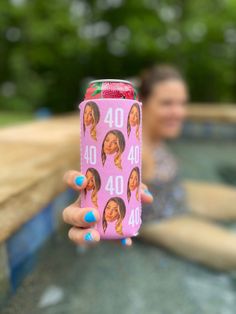 a woman holding up a pink can with photos on it