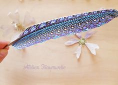 a hand holding a blue and white feather on top of a table next to flowers