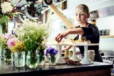 a woman standing in front of a counter filled with lots of vases and flowers