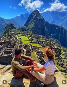 two people sitting on top of a mountain looking at the view over machu ruins