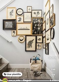 a bunch of pictures hanging on the wall next to a handbag and purse in front of some stairs