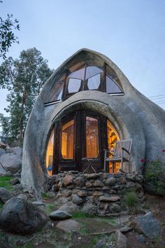 an unusual looking house made out of rock and glass with a chair in the window