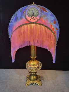 a colorful lamp with fringes on it and a clock in the middle is sitting on a table