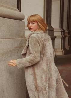 a woman leaning against a pillar wearing a coat