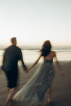 a man and woman walking on the beach holding hands