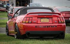 the rear end of a red sports car parked in front of other cars on grass