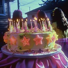 a birthday cake with stars and candles on it in front of two girls looking at the camera