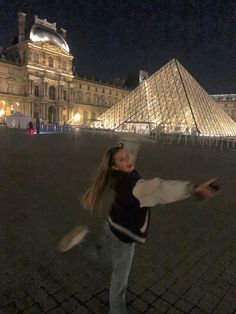 a woman is throwing a frisbee in front of a large building at night