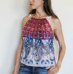 a woman standing in front of a white wall wearing a red and blue top with paisley print