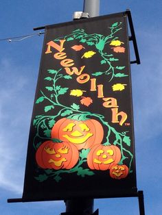 a black sign with pumpkins on it hanging from the side of a street light