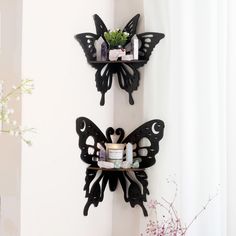 two black butterfly shaped wall shelves on the side of a white wall next to a vase with flowers