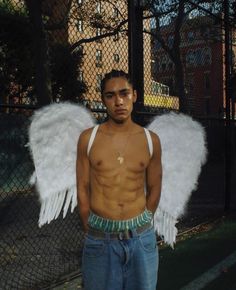 a shirtless man with large white wings on his chest standing in front of a fence