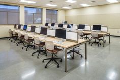 an empty room with desks and computer screens on the tables in front of large windows