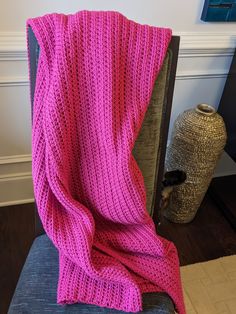 a pink knitted blanket sitting on top of a blue chair next to a vase