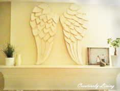 an angel wing sculpture on top of a mantel above a mantle with potted plants