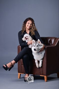 a woman sitting in a chair with two dogs on her lap and smiling at the camera