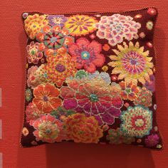 a decorative pillow is displayed on a red surface with an orange wall in the background