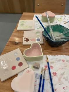 the table is covered with art supplies such as paint, brushes and heart shaped dishes