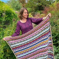 a woman holding up a multicolored crocheted blanket