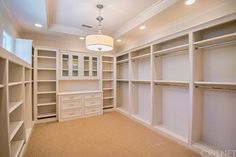 an empty walk in closet with lots of white shelves and drawers on either side of the closet