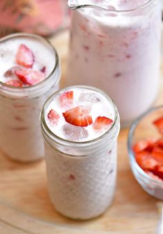 three jars filled with strawberries and ice cream on top of a wooden table next to two bowls full of strawberries