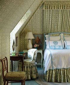 a bed sitting under a window next to a chair and table in a room with white walls