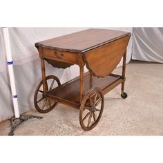 an old wooden cart with wheels and a table on the bottom, sitting in front of a white wall